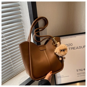 Close-up of matte brown leather tote bag with vertical stitching and plush toy charm