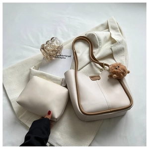 Detail of cream tote bag with brown trim, matching pouch, and monster charm