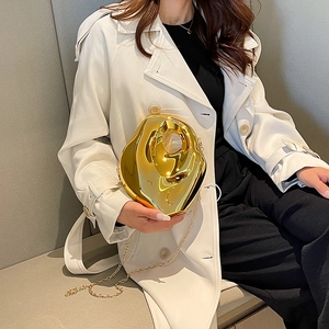 Irregular fluid gold evening clutch with chain strap shown on model in white coat