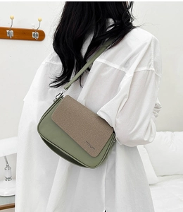 Detail of grey-green leather crossbody bag with brown woven flap on white shirt