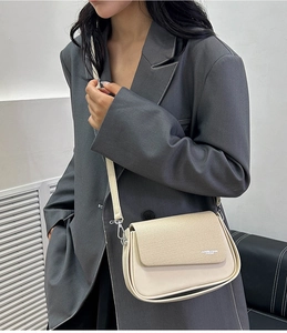 Detail of cream flap crossbody bag with adjustable strap worn on a grey blazer