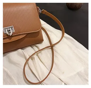 Detail of a brown pleated crossbody bag showing the silver metal lock and thin shoulder strap