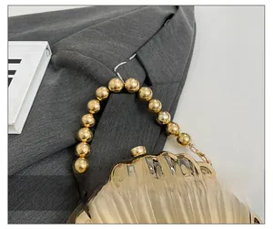 Detail of golden shell evening bag with beaded handle and glossy wave texture