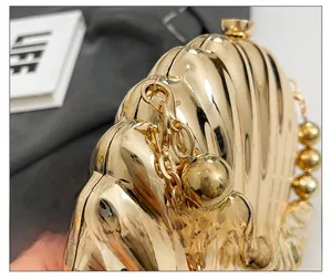 Close-up of golden shell-shaped evening bag with glossy metallic finish and beaded handle