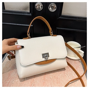 Detailed view of white textured leather handbag with silver lock and brown strap