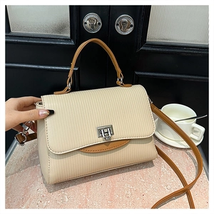 Detail of cream striped handbag with brown leather handles and silver metal flip lock