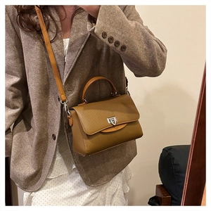 Detail of tan brown handbag featuring vertical stripe texture and silver metal twist lock