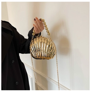 Close-up of shell-shaped gold acrylic evening bag with beaded handle and chain strap