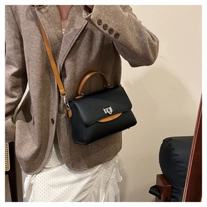 Detail of a black textured crossbody bag with brown handles and silver twist lock closure