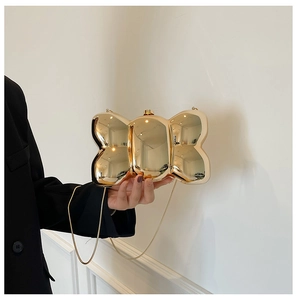 Detail view of a gold bow-shaped clutch with a reflective mirror finish and chain