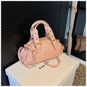 Close-up of pink shell handbag with gold buckle handles and decorative rivets detail