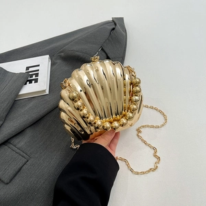 Glossy gold shell-shaped clutch bag with pearl bead trim and chain strap on grey blazer