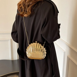 Golden acrylic shell evening bag with metallic finish and chain strap on a model