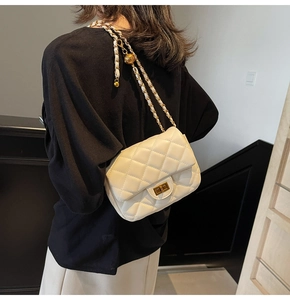 Detail view of white quilted crossbody bag featuring a gold ball adjustment and chain strap