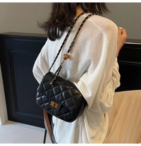 Detail of black quilted chain bag with gold metal adjustment ball worn by a model