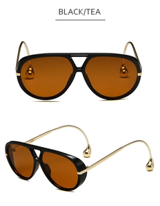 Detalle de gafas aviador con montura negra, lentes de té y patillas con gotas doradas