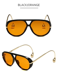 Detalle de gafas de sol aviador con montura negra, lentes naranjas y patillas doradas