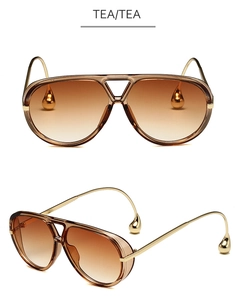 Detalle de gafas de sol aviador doradas con lentes degradados té y colgante gota