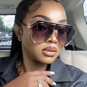 Detail of oversized gold metal sunglasses with purple gradient lenses worn by a model