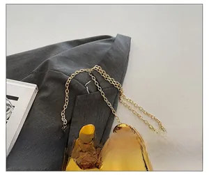Close-up of golden chain strap attachment on glossy pig-shaped acrylic evening bag