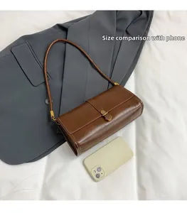Brown patent leather underarm bag shown next to a smartphone for size comparison