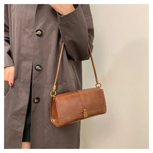 Brown vintage leather baguette bag shown as a shoulder bag on a model in a long coat