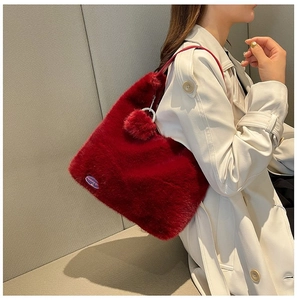 Detail of dark red faux fur tote bag with pompom charm on a model in a trench coat