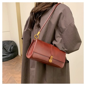 Detail of burgundy leather shoulder bag with gold metal buckle shown on a model