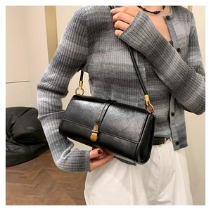 Close-up of minimalist black baguette handbag with gold metal clasp on model's shoulder