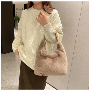 Detail of khaki plush handbag with leather strap and decorative pompom charm on side