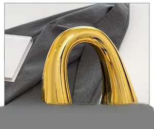 Detailed macro view of the ergonomic polished gold metal handle on a stylish handbag