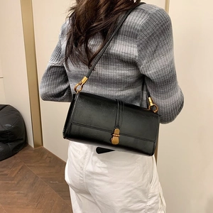 Modern black leather shoulder bag with gold hardware worn by a person in a cozy interior