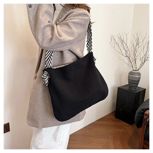 Dettaglio della borsa tote in velluto nero con tracolla a righe e occhielli in metallo annodati