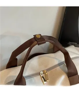 Detail of canvas travel bag featuring brown straps, leather snap and golden double zippers