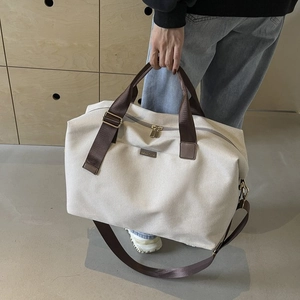 Detail of a large canvas travel bag featuring brown straps and dual golden zippers