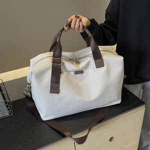 Detail of canvas travel bag with brown nylon handles and metal logo plate on white fabric