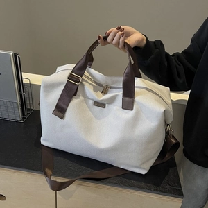 Detail of grey canvas tote bag featuring brown straps, leather logo, and gold metal hardware