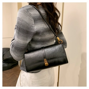 Minimalist black faux leather baguette bag with vintage bronze buckle on shoulder