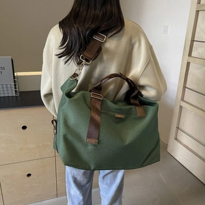 Detail of dark green canvas travel bag with wide brown shoulder strap and leather handles