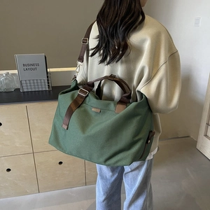 Detailed view of dark green canvas shoulder bag with brown straps and metal hardware detail