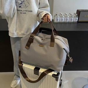 Gray travel tote bag with brown straps secured on a white suitcase handle for easy travel