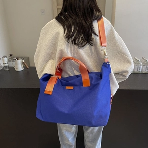 Detail of royal blue canvas tote with contrast orange straps shown in a cafe setting