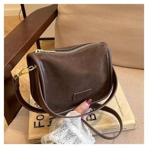 Detailed view of the dark brown suede saddle bag with gold zipper and long strap on books