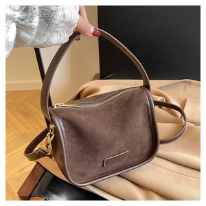 Detailed view of brown suede handbag with top zipper and gold metal strap hardware
