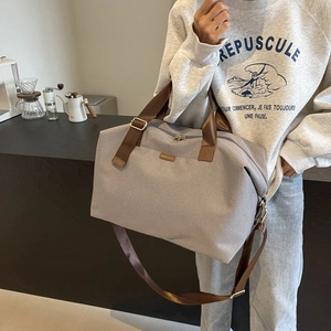Model wearing large grey canvas travel duffle bag with brown straps in a cafe setting