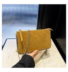 Close-up of yellow suede crossbody bag with silver metal studs and chain strap