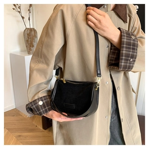 Detail of a black semicircular crossbody bag with matte suede and leather stitching