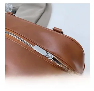 Detail view of smooth brown leather shoulder bag featuring a silver metal zipper and stitching
