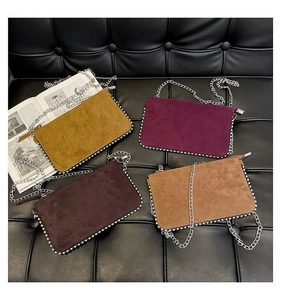 Flat lay of colorful suede crossbody bags with metal chain edges on a leather backdrop