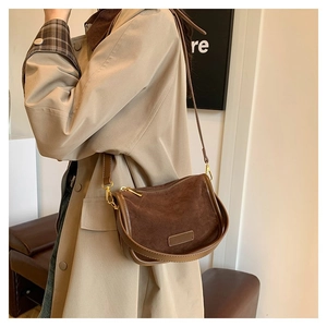 Detail of a brown suede half-moon crossbody bag with smooth leather trim on a beige coat